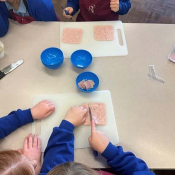 Children helping eachother cutting meat to make homemade pizzas